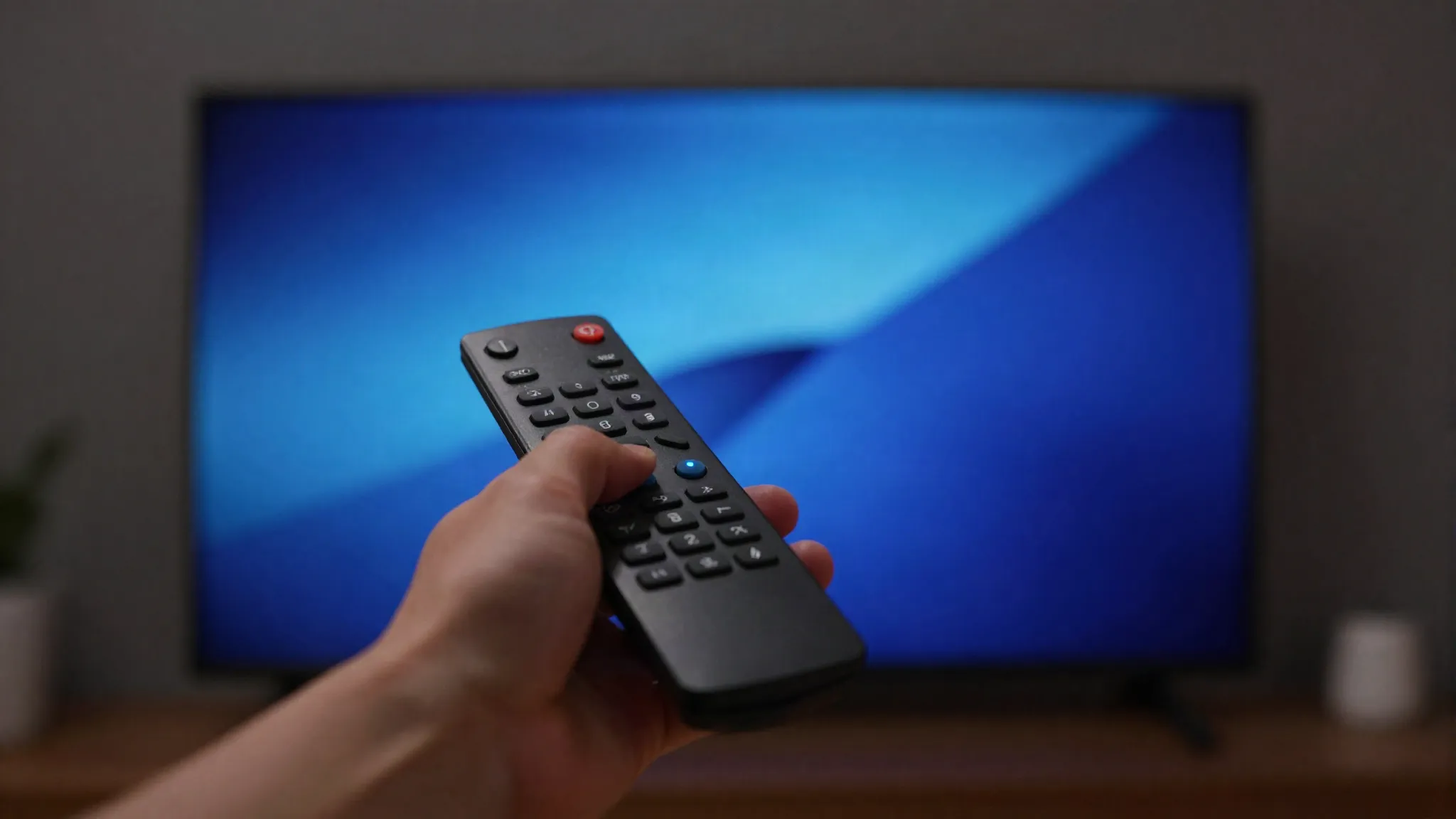 Main tenant une télécommande devant un téléviseur allumé dans un salon sombre