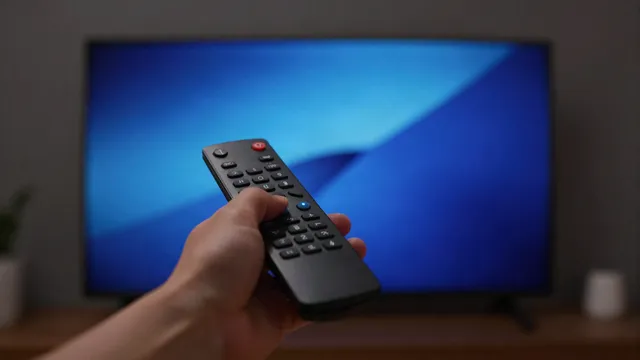 Main tenant une télécommande devant un téléviseur allumé dans un salon sombre